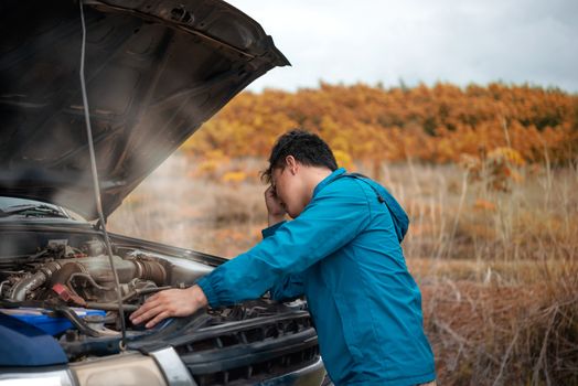 Asian stressed man having trouble with his broken car looking in frustration at failed engine