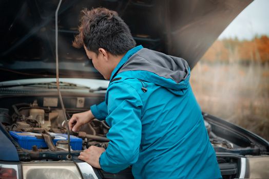 Asian stressed man having trouble with his broken car looking in frustration at failed engine