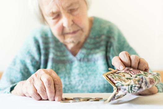 Concerned elderly 96 years old woman sitting at table at home and counting remaining coins from pension in her wallet after paying bills. Unsustainability of social transfers and pension system.