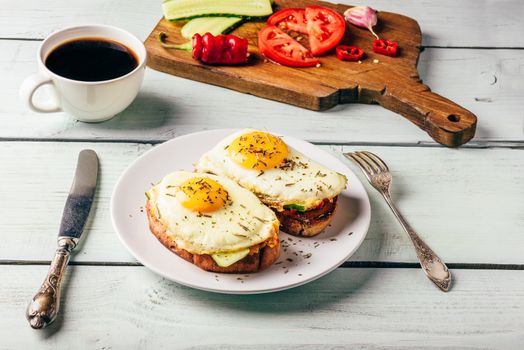 Breakfast toasts with vegetables and fried egg on white plate, cup of coffee and some fruits over wooden background. Clean eating food concept.