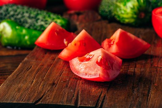 Sliced tomatoes on cutting board and cucumbers with chili peppers over wooden background.