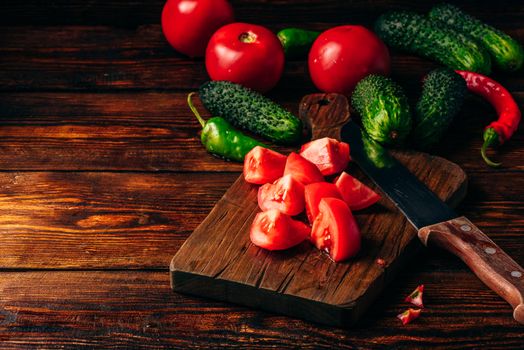 Sliced tomatoes on cutting board and cucumbers with chili peppers over wooden background.