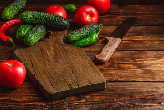 Fresh cucumbers, tomatoes and chili peppers on cutting board for preparing salad.