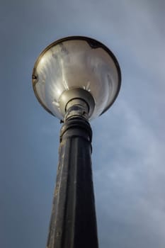 Old decorative black streetlamp standing vertically below the blue sky