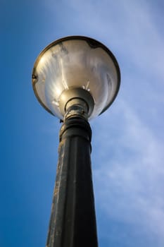 Old decorative black streetlamp standing vertically below the blue sky