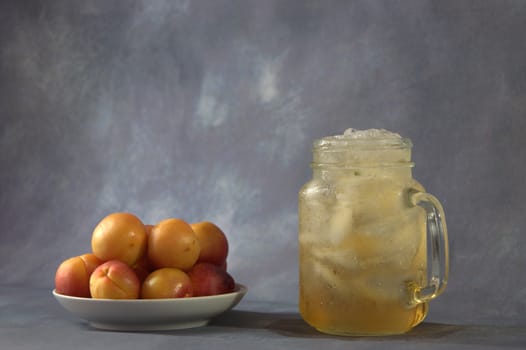 A few fresh apricots on a plate and a cup of apricot juice with ice.