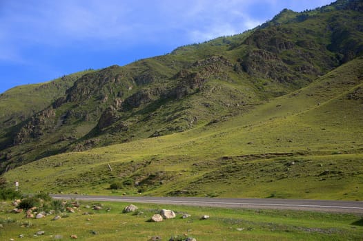 Asphalt road going through a green valley sandwiched between the mountains. Altai, Siberia, Russia.