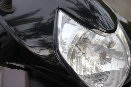 Close up of the headlamp of a black scooter resting with head tilted