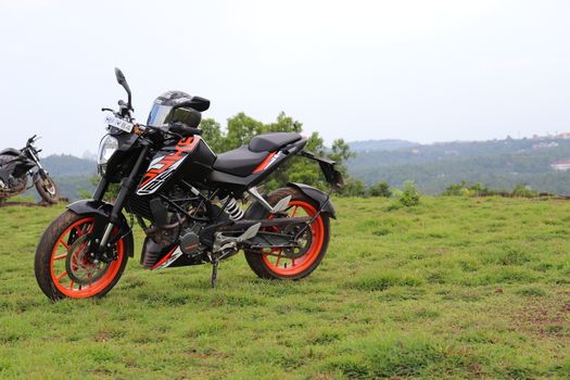 An orange sports motor bike resting on a green hill with beautiful mountains in the background