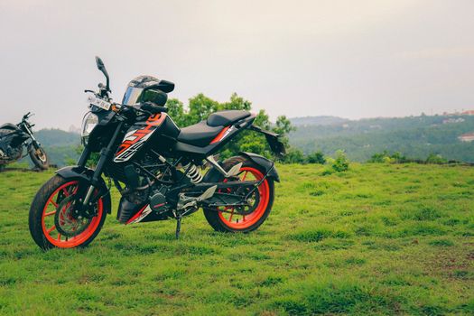An orange sports motor bike resting on a green hill with beautiful mountains in the background