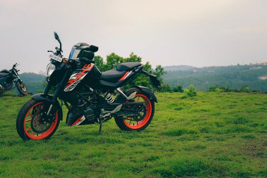 An orange sports motor bike resting on a green hill with beautiful mountains in the background