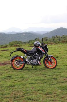 An orange sports motor bike resting on a green hill with beautiful mountains in the background