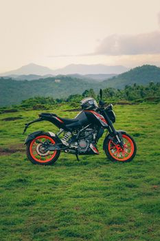 An orange sports motor bike resting on a green hill with beautiful mountains in the background