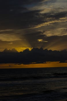 Orange sky with rays of sun coming from the backside of the cloud above the sea