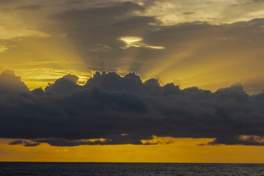 Orange sky with rays of sun coming from the backside of the cloud above the sea