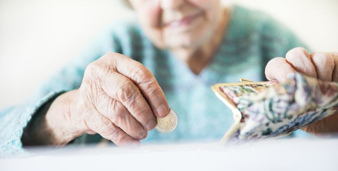 Detailed closeup photo of elderly 96 years old womans hands counting remaining coins from pension in her wallet after paying bills. Unsustainability of social transfers and pension system.