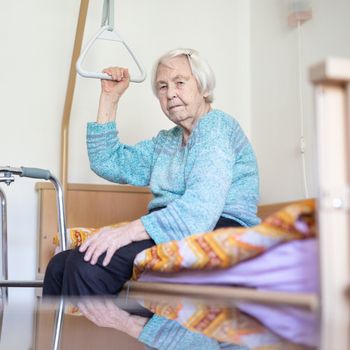 Elderly 96 years old woman sitting on medical bed in hospic. Palliative health care support for older people concept. Care for the elderly.