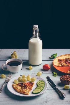 Frittata and fruits, vegetables, bottle of milk, cup of coffee over light wooden background. Healthy breakfast concept.