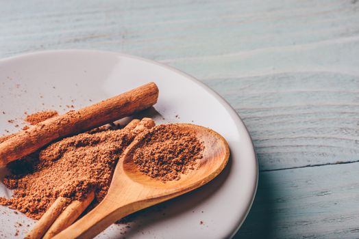 Cinnamon sticks and ground spice on white plate over light wooden background.