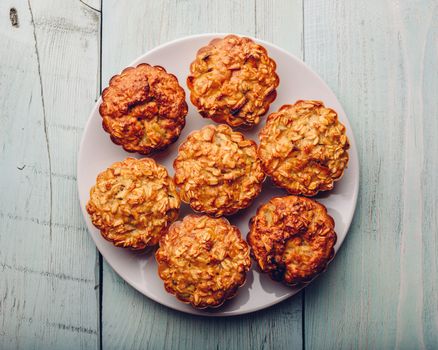 Cooked oatmeal muffins on white plate over light wooden background. View from above.