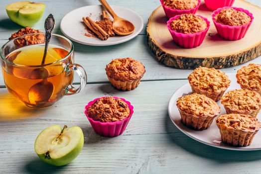 Healthy Breakfast. Cooked oatmeal muffins with apple and cup of green tea over light wooden background.