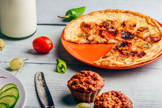 Frittata with chorizo, tomatoes and chili peppers on plate and muffins over light wooden background.