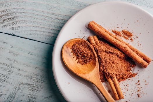 Cinnamon sticks and ground spice on white plate over light wooden background. View from above.