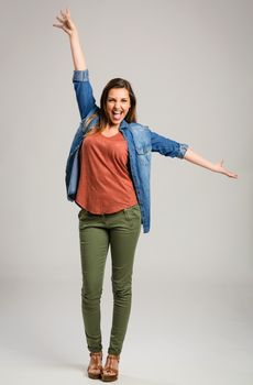 Beautiful happy woman with arms up over a gray background