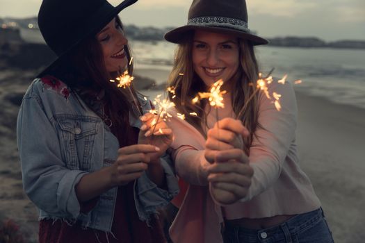 Two best friends celebrating, holding sparklers at beach 