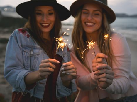 Two best friends celebrating, holding sparklers at beach 