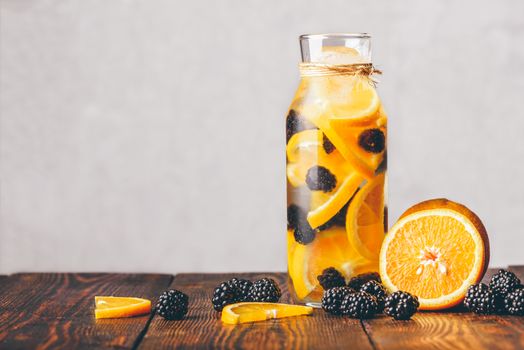 Bottle of Water Infused with Sliced Raw Orange and Fresh Blackberry. Ingredients on Wooden Table.