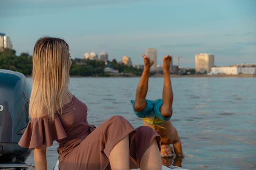 The guy jumps into the water from the boat. A beautiful girl is watching him