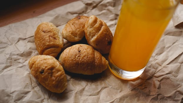 Freshly baked croissants with orange juice on kraft paper. Closeup photography of fresh delicious dessert for breakfast.