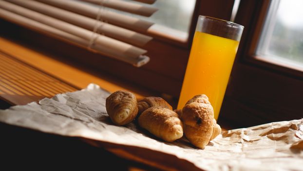 Freshly baked croissants with orange juice on kraft paper. Closeup photography of fresh delicious dessert for breakfast.