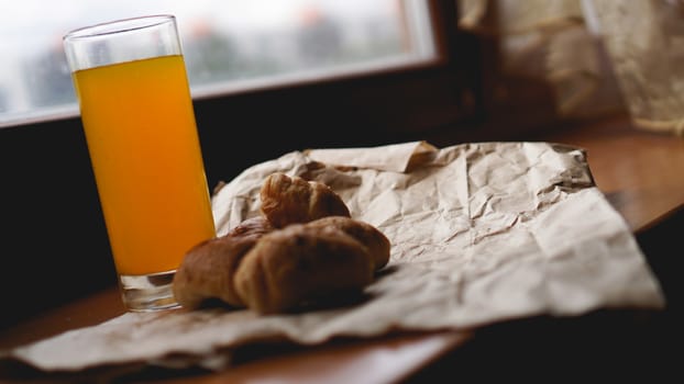 Freshly baked croissants with orange juice on kraft paper. Closeup photography of fresh delicious dessert for breakfast.