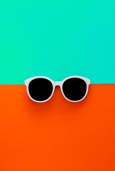 Sunny stylish white sunglasses on a bright blue-cyan and red-orange background, top view, isolated. Copy space. Flat lay.