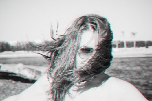 A young girl in sunglasses laughs, her hair covers her face, the wind. Effekt glitch anaglyph. Black and white monochrome. Retro photo