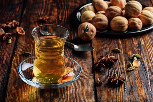 Spiced tea with star anise, cardamom and dried lime in armudu glass over wooden surface