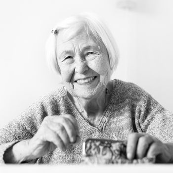 Cheerful elderly 96 years old woman sitting at table at home happy with her pension savings in her wallet after paying bills. Saving for retirement and financial planing concept. Black and white.