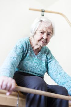 Elderly 96 years old woman exercising with a stick sitting on her bad. Geriatric health care home assisted support for older people concept. Care for the elderly.