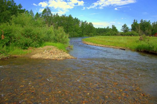 The rocky bottom of the shallow Ursul River flowing in is surrounded by forests and mountains. Altai, Siberia, Russia.