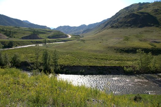 Reflection of a rising sun in a river flowing through a mountain valley. Altai, Siberia, Russia.