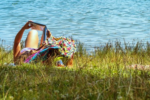 A girl lies in a river and reads a book. Young woman reading a book sitting by the river.