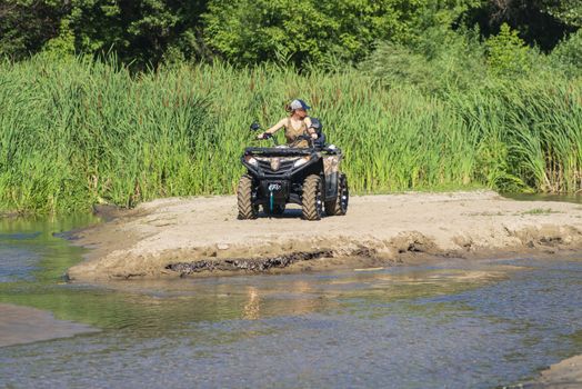 A girl on a Quad bike riding on the beach. A happy woman riding a quad bike on the river.