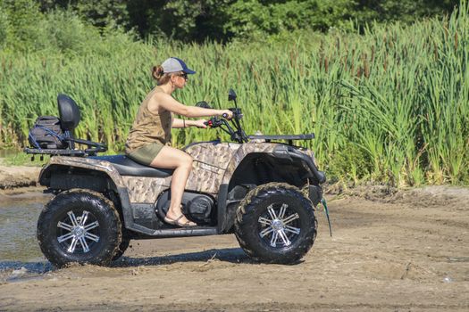 A girl on a Quad bike riding on the beach. A happy woman riding a quad bike on the river.