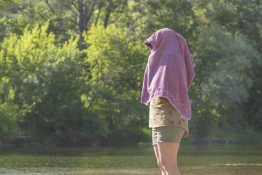 The girl hid her face from the bright sun under a towel.The girl is sitting on the beach with a towel on her head.