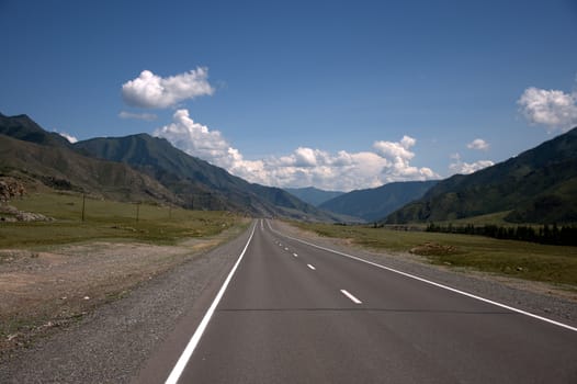 Asphalt road running through the valley and leaving the horizon surrounded by mountains. Altai, Siberia, Russia.
