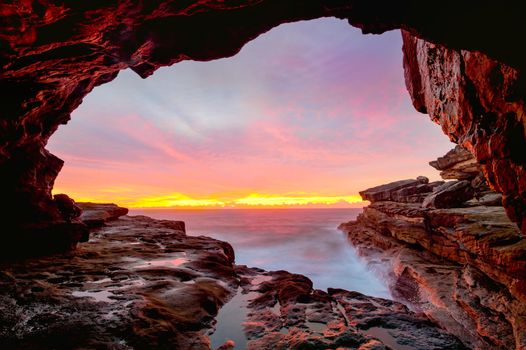 Coastal cave arch views to glorious full colour sunrise over the ocean.  Long exposure creates a mystical affect of the waves motion around the rocks
