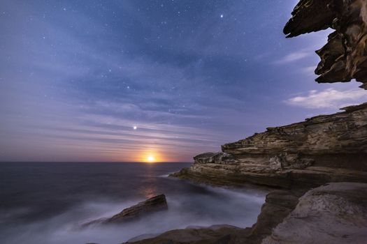 Sydney coastal cliffs by night with moonrise and light high clouds rippling in the sky like waves on the ocean