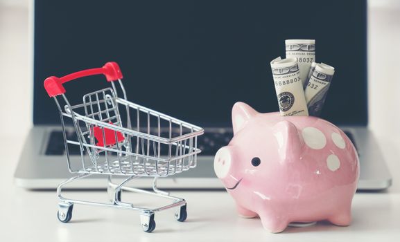 shopping cart and piggy bank with laptop on the desk, online shopping concept